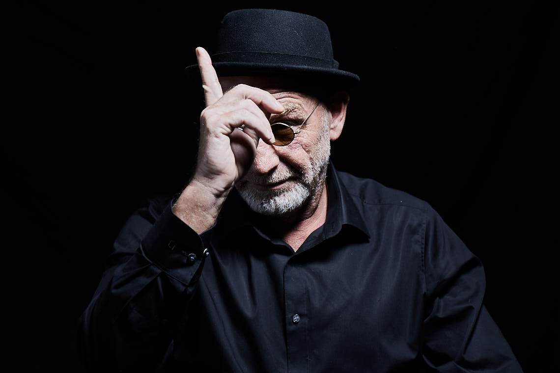 Udo Böhr mit Hut und runder Sonnenbrille, tippt an die Hutkrempe